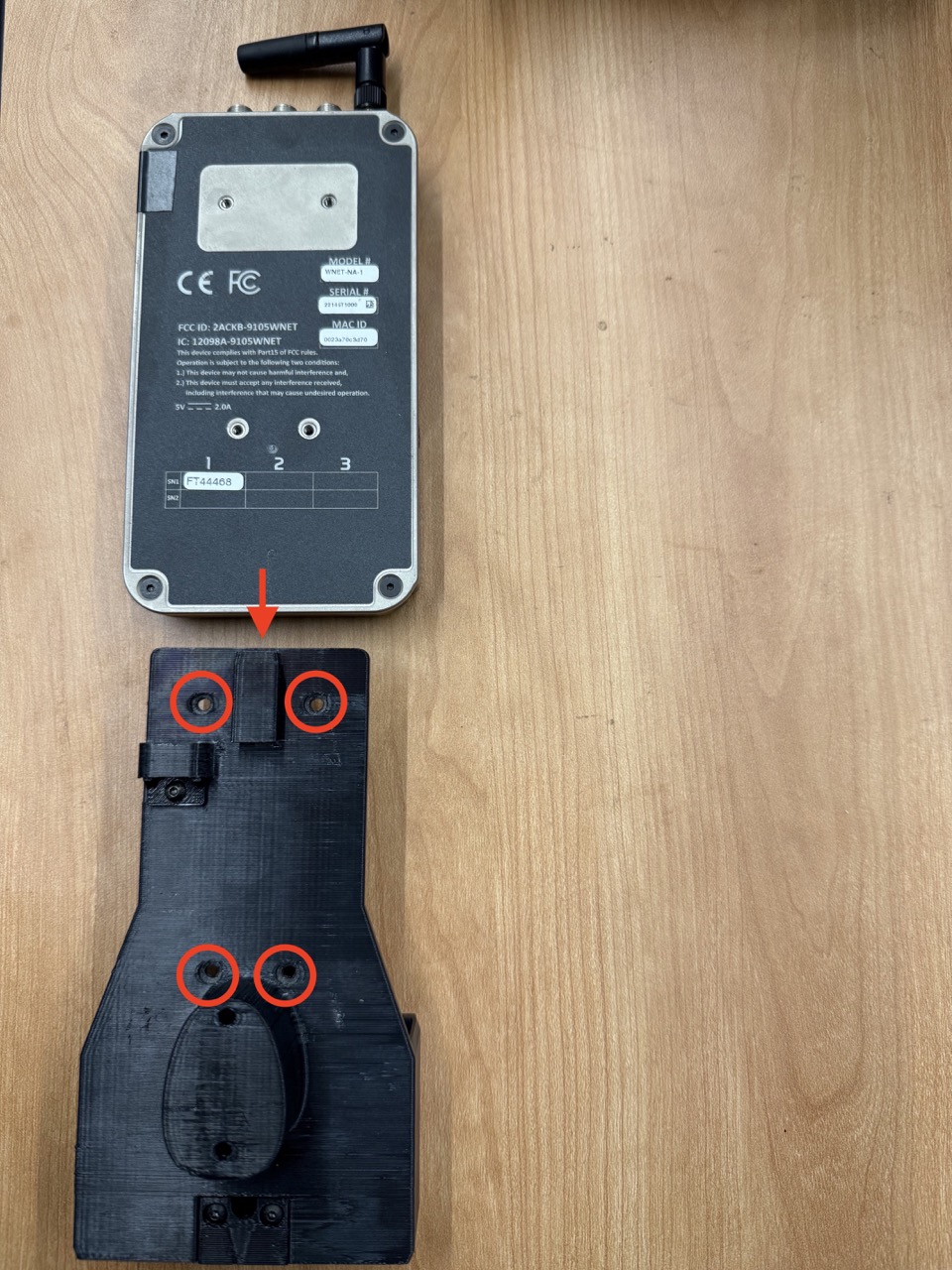 
                    This figure shows a picture of the wireless F/T mount and the
                    wireless F/T transmitter, with an arrow indicating how the
                    transmitter slides into the mount. The locations where the screws
                    attach are circled in red.
                    