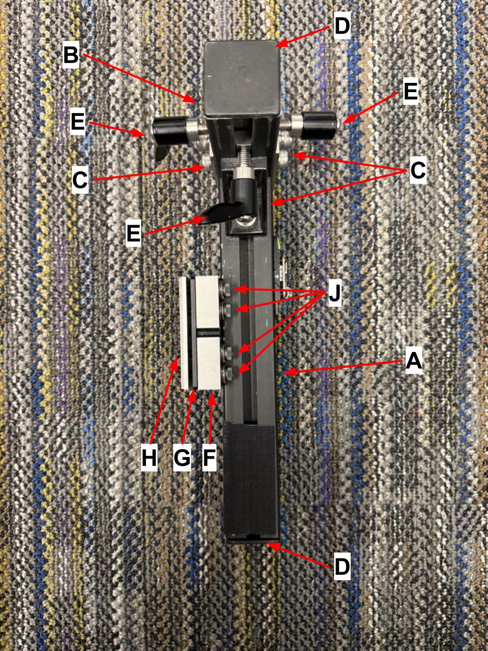 
                    The top view of the wheelchair mount, with letters corresponding
                    to the items in the parts list.
                    