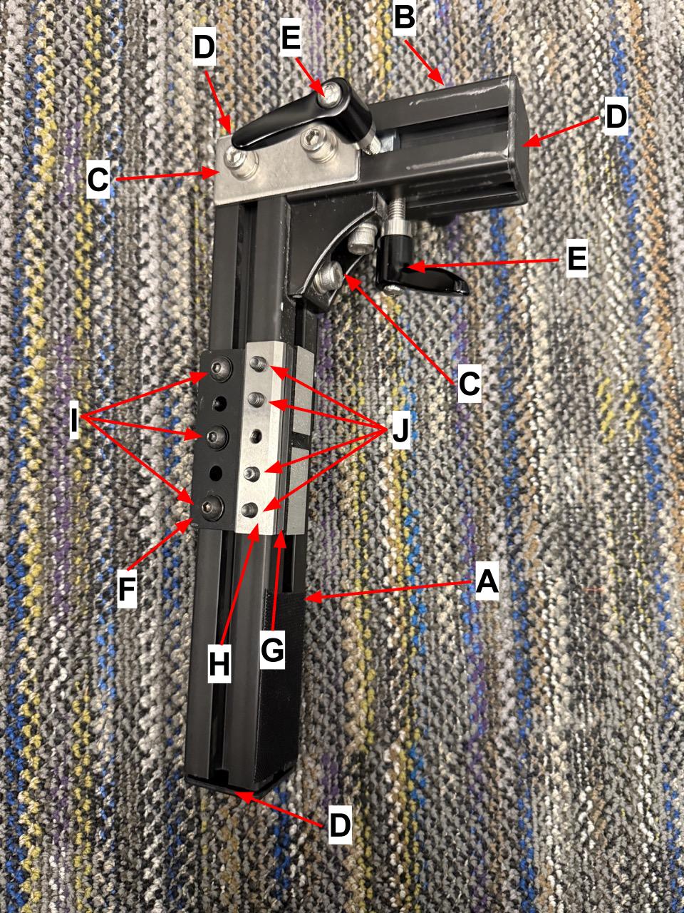 
                    The back view of the wheelchair mount, with letters corresponding
                    to the items in the parts list.
                    